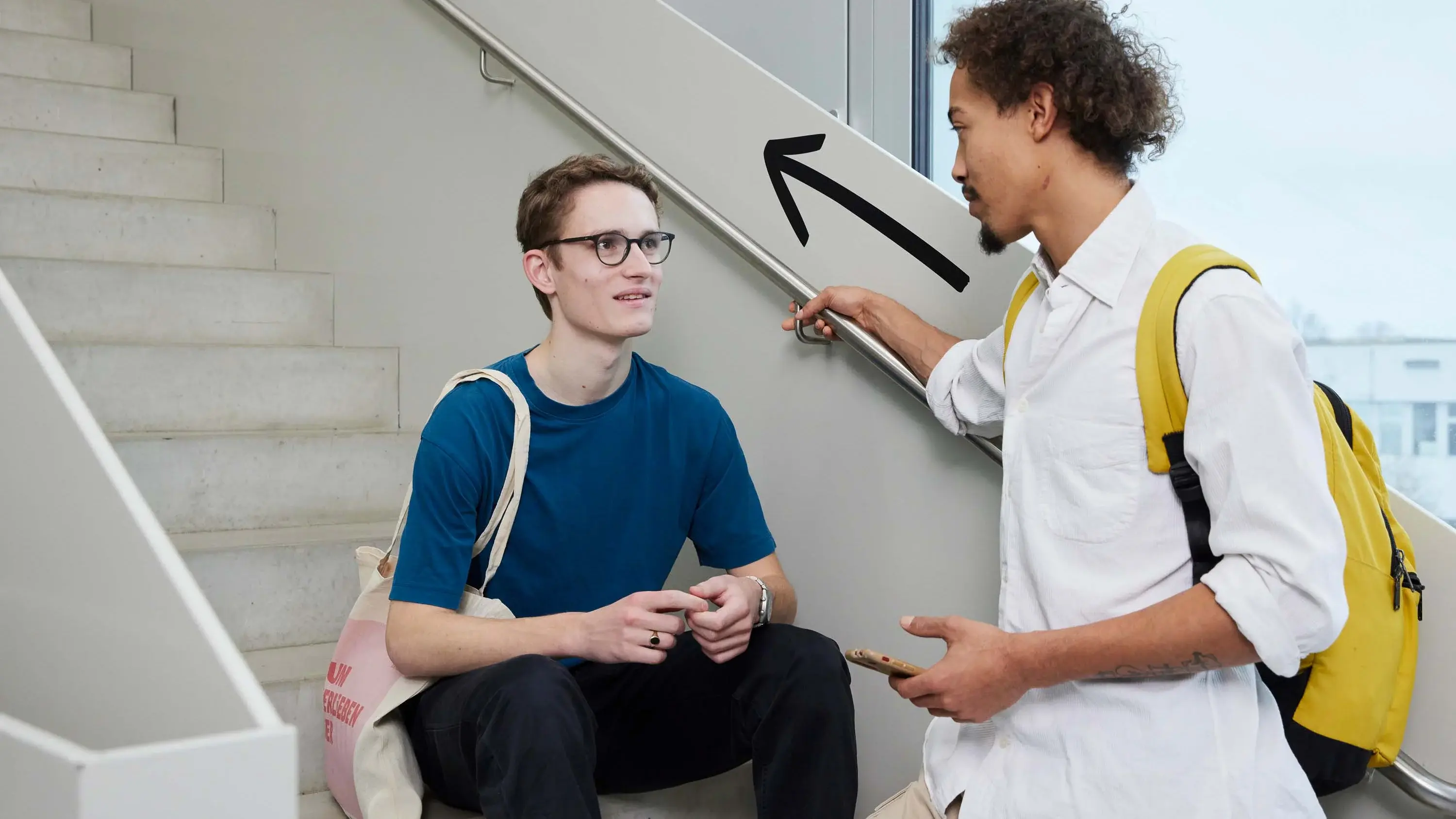 Studierende sitzen auf einer Treppe und unterhalten sich.